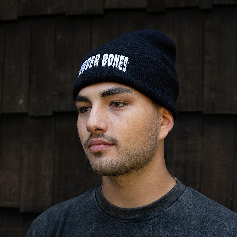 On-body 3/4 view of Rubber Bones Black Beanie showcasing embroidered logo.