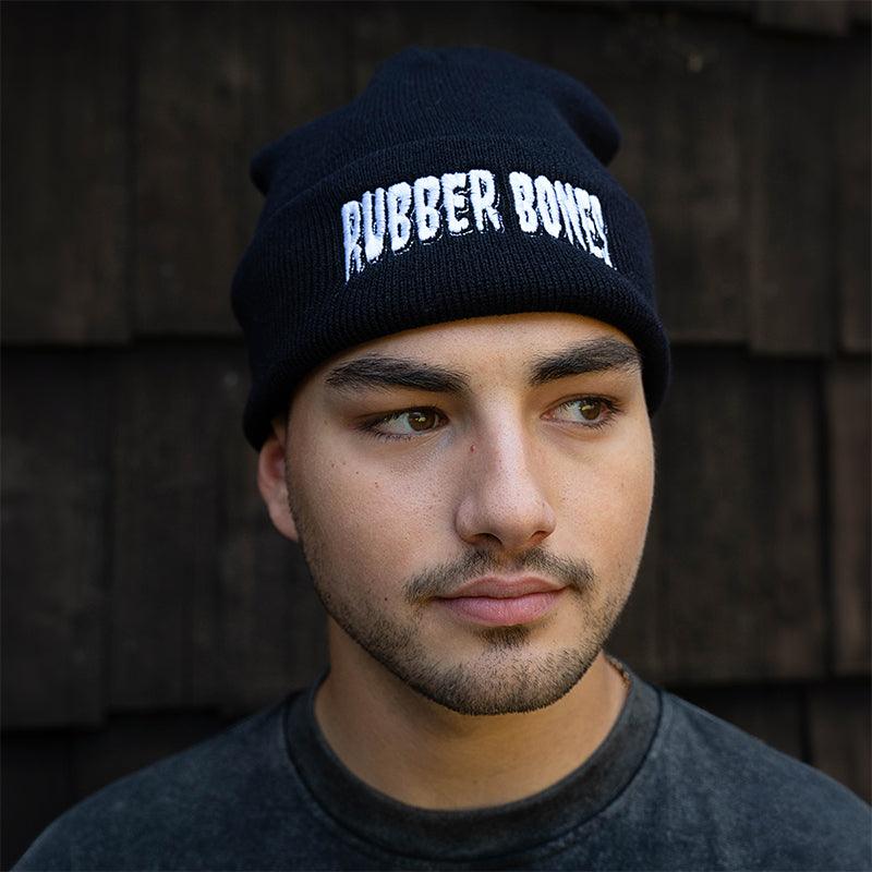On-body front view of Rubber Bones Black Beanie with embroidered logo.
