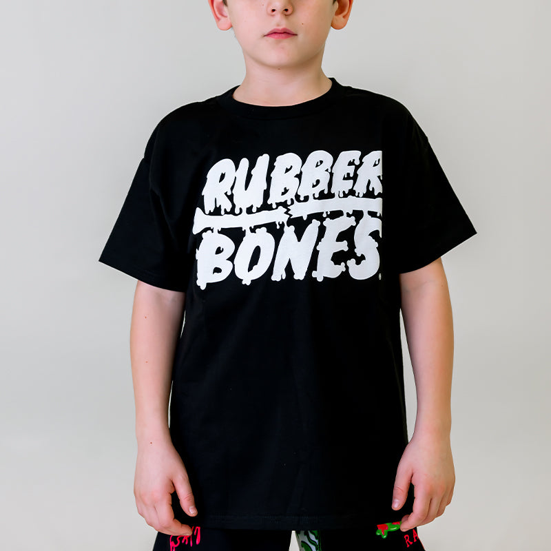 Front view. Kid model wearing Rubber Bones black t-shirt with white Rubber Bones Logo screen printed on center chest.