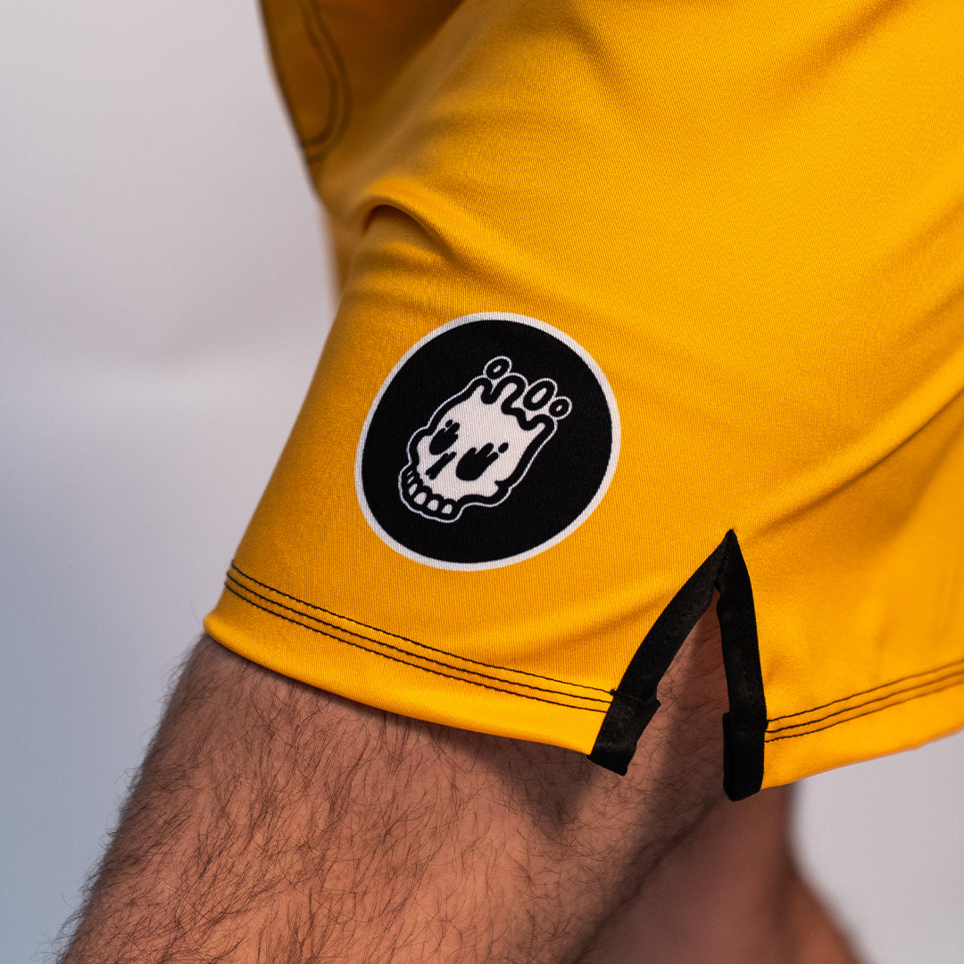 Volt Ranger BJJ Shorts (Leg Logo Detail) – A close-up of the small black-and-white Rubber Bones skull patch on the lower left leg of the yellow BJJ shorts.