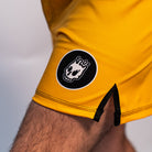 Volt Ranger BJJ Shorts (Leg Logo Detail) – A close-up of the small black-and-white Rubber Bones skull patch on the lower left leg of the yellow BJJ shorts.