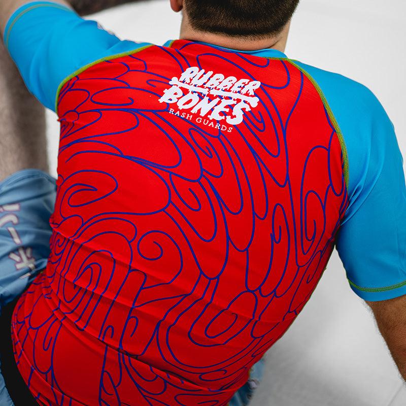 On-body shot of Hannya Drip Rash Guard in red with blue sleeves, paired with matching grappling shorts, back view.