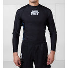 Model wearing the Men’s Long Sleeve Ash BJJ Rash Guard featuring black body, white Rubber Bones logo, and gray marble side detailing.