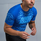 On-body 3/4 view of Ranked Rash Guard - Blue sleeve with Rubber Bones logo and monochromatic skull web pattern.