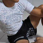 On-body seated athlete wearing full competition set with Ranked Rash Guard - White and black competition grappling shorts.