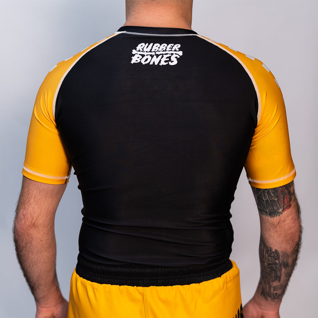 Volt Ranger Rash Guard on Model (Back) – A male model wearing the Volt Ranger BJJ rash guard, highlighting the fit with the "Rubber Bones" logo on the upper back and yellow sleeves with a checkerboard pattern.