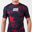 Model wearing the Ember Men’s BJJ Rash Guard in red and black tie-dye design with white Rubber Bones logo on front.