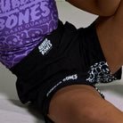 On-body seated view of Competition Grappling Shorts, close-up of the front with black and white IBJJF-approved design.