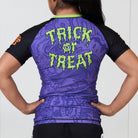 Back of Trick or Treat women’s BJJ rash guard featuring green slime text and Halloween-themed background artwork.