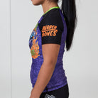Side view of purple and black Trick or Treat women’s rash guard with orange Rubber Bones logo on sleeve.