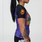 Side view of women’s Trick or Treat rash guard showing orange skull logo and vivid Halloween art.