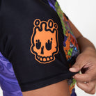 Close-up of orange Rubber Bones skull logo printed on black sleeve of Trick or Treat BJJ rash guard.