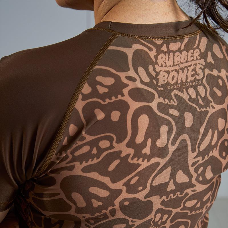 On-body 3/4 back close-up of Women's Brown Ranked Rash Guard highlighting the Rubber Bones logo.
