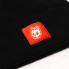 Close up of black cuff beanie with white Rubber Bones Icon logo on a red patch.