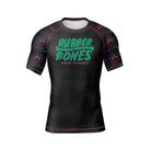 Black short-sleeve BJJ rash guard with a bold green and pink 'Rubber Bones Rash Guards' logo across the chest. Sleeves feature a dripping neon smiley face pattern, creating a vibrant and edgy look.