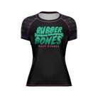 Black women's short-sleeve BJJ rash guard with a neon green and pink 'Rubber Bones Rash Guards' logo on the chest. Sleeves feature a psychedelic melting smiley face design, blending vibrant colors.