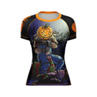 Halloween-inspired women's short-sleeve BJJ rash guard featuring a detailed illustration of a sinister pumpkin-headed scarecrow looming over a defeated zombie clown under a full moon. The black base is accented with orange branding and stitching.