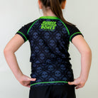 Bad Bones Kids BJJ Rash Guard, back view, showcasing green rubber bones logo on black fabric with a grey skull pattern and green stitching.