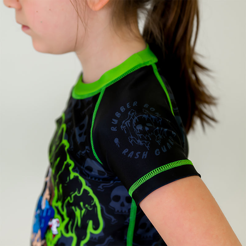 Bad Bones Kids BJJ Rash Guard, left side view, highlighting black sleeve with grey skull logo and green stitching.