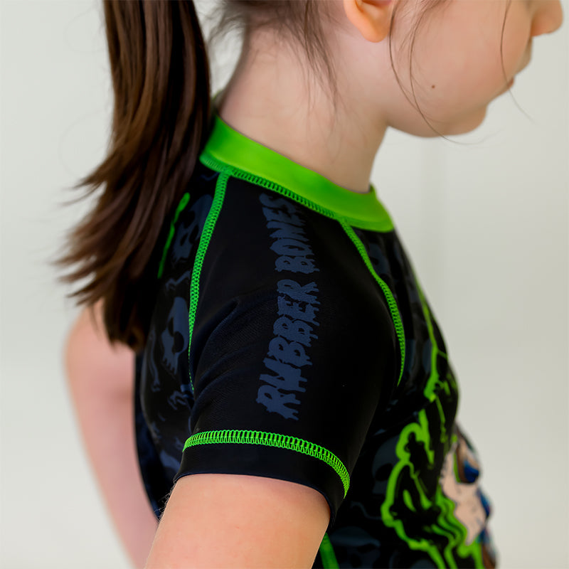 Bad Bones Kids BJJ Rash Guard, right side view, black sleeve featuring grey Rubber Bones logo with green stitching.