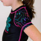 Bubble Gum Kids BJJ Rash Guard, left side view, highlighting purple, green, and pink dripping alien smiley faces on the sleeve with a black body