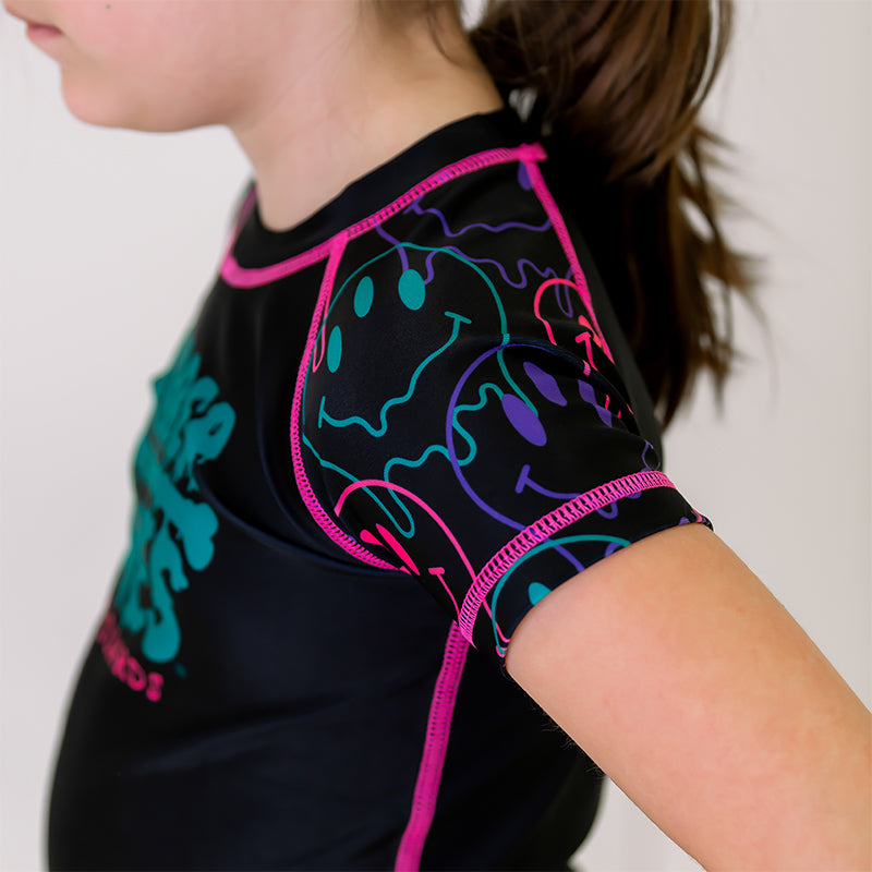 Bubble Gum Kids BJJ Rash Guard, left side view, highlighting purple, green, and pink dripping alien smiley faces on the sleeve with a black body