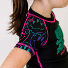 Bubble Gum Kids BJJ Rash Guard, right side view, highlighting purple, green, and pink dripping alien smiley faces on the sleeve with a black body