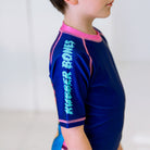 Close-up of the right sleeve of the Kids BJJ Invasion Rash Guard, featuring Rubber Bones logo.