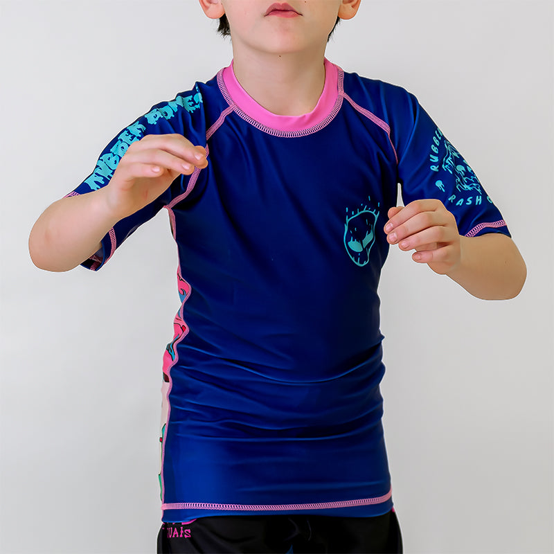 Kids BJJ Invasion Rash Guard, front view, featuring a blue body with an alien head design on the left chest and pink stitching.