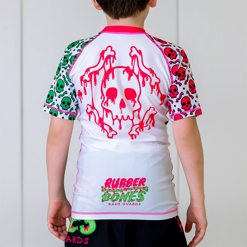 OG Kids BJJ Rash Guard, back view, featuring a white back with a pink dripping skull design and pink and green Rubber Bones logo at the bottom.