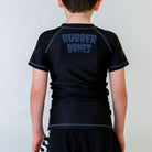 Kids Pumpkin Pie BJJ Rash Guard, back view, black with a grey Rubber Bones logo at the nape of the neck and grey stitching.