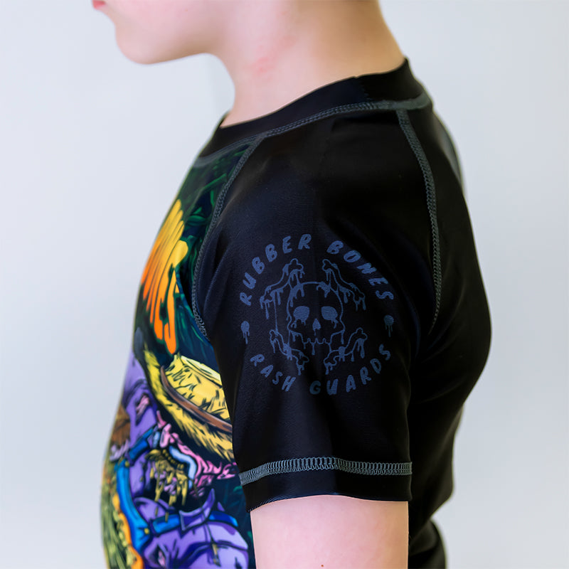 Close-up of the left sleeve of the Kids Pumpkin Pie BJJ Rash Guard, black with a grey Rubber Bones logo and grey stitching.