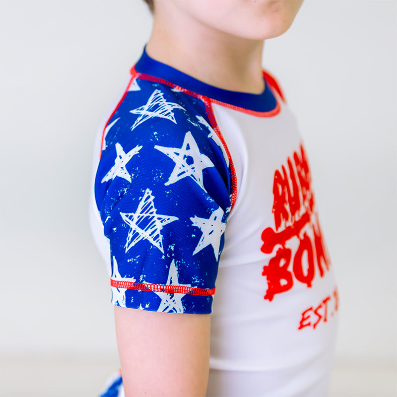 Independence Kids BJJ Rash Guard, right side view, highlighting white distressed stars on the right sleeve with a blue body.