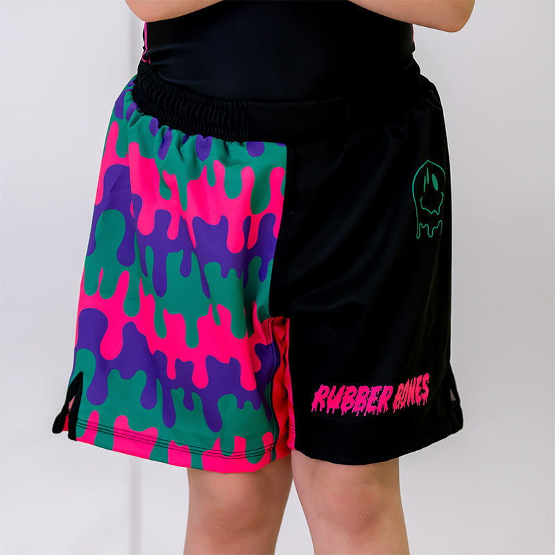 Bubble Gum Kids BJJ Shorts, front view, featuring black shorts with a purple, pink, and green drip pattern on the right side, and a green dripping smiley-faced alien with a pink Rubber Bones logo on the left side.