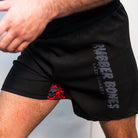 Action shot of black BJJ fight shorts featuring a gray "Rubber Bones Rash Guards" logo on the left leg. Skull-patterned red inner panel partially visible. Mid-motion, emphasizing flexibility.