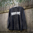 Black Long Sleeve Acid Wash T-Shirt with white Rubber Bones logo, hanging from a fence.