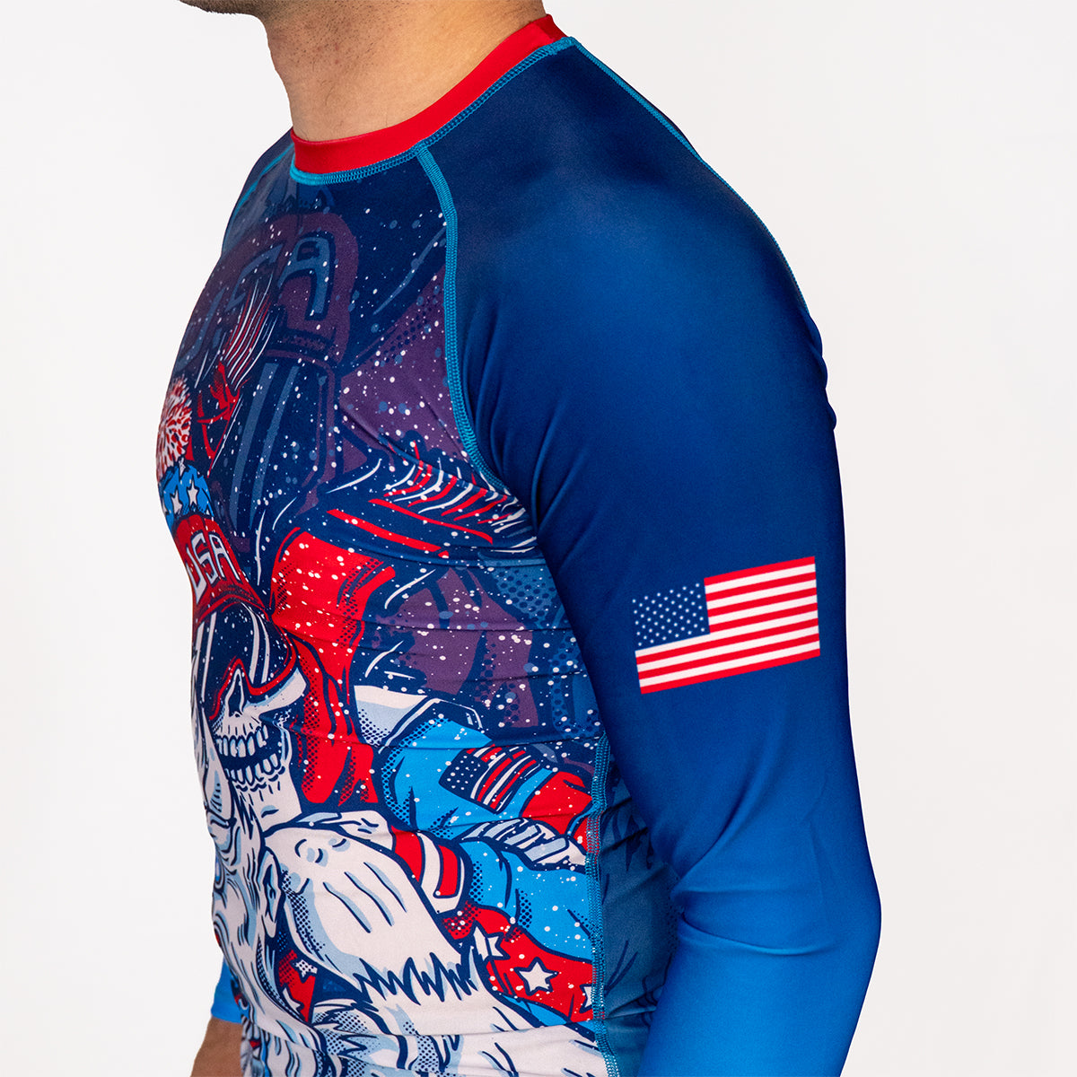 Side profile of Men's Yeti Games long sleeve rash guard showing complete skeleton skier Yeti artwork, USA flag on sleeve, blue compression sleeves, and athletic fit for no gi BJJ.