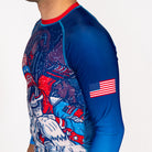 Side profile of Men's Yeti Games long sleeve rash guard showing complete skeleton skier Yeti artwork, USA flag on sleeve, blue compression sleeves, and athletic fit for no gi BJJ.