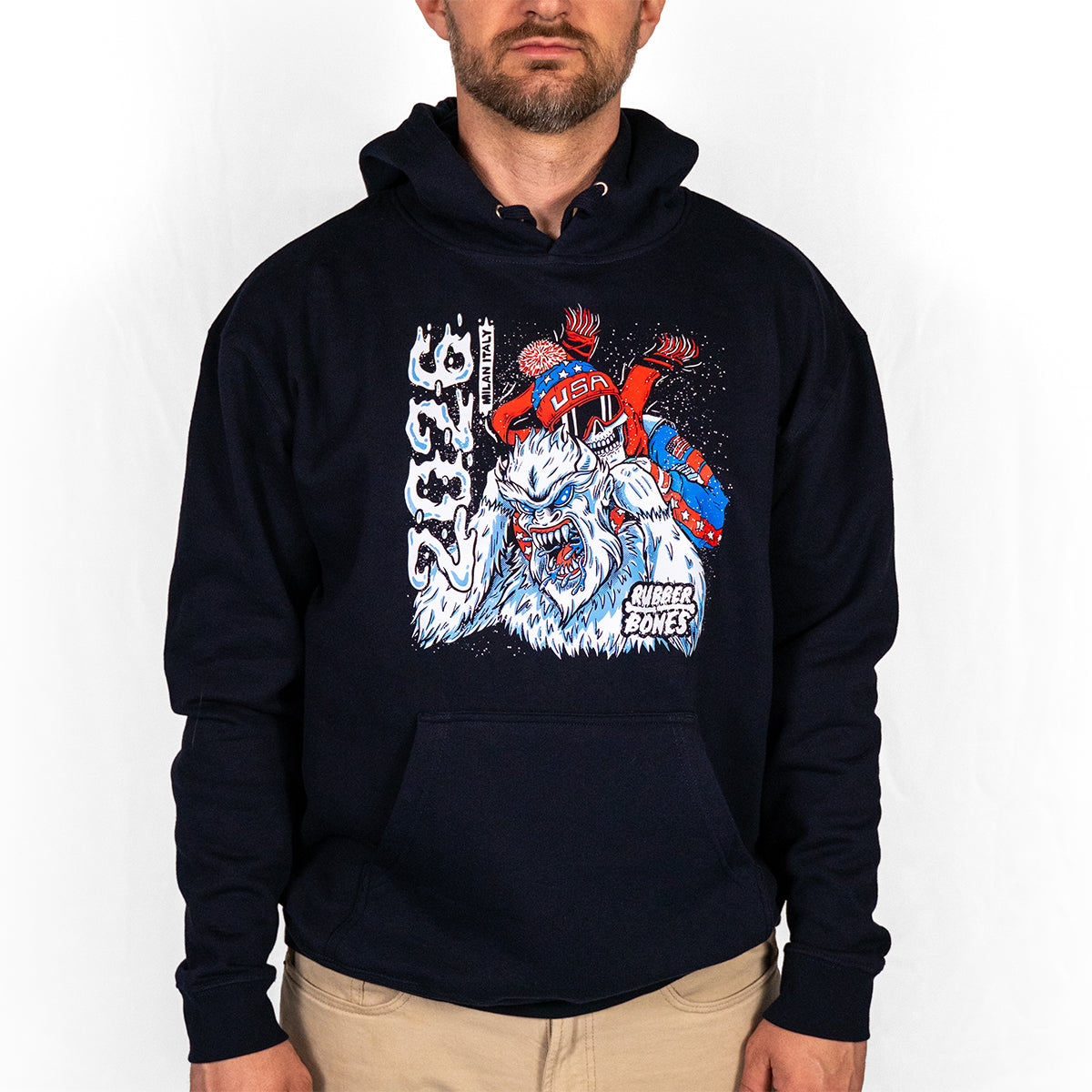 Man wearing navy Yeti Games hoodie with skeleton skier choking Yeti artwork in red, white, and blue on chest, double-drawstring hood, kangaroo pocket visible.