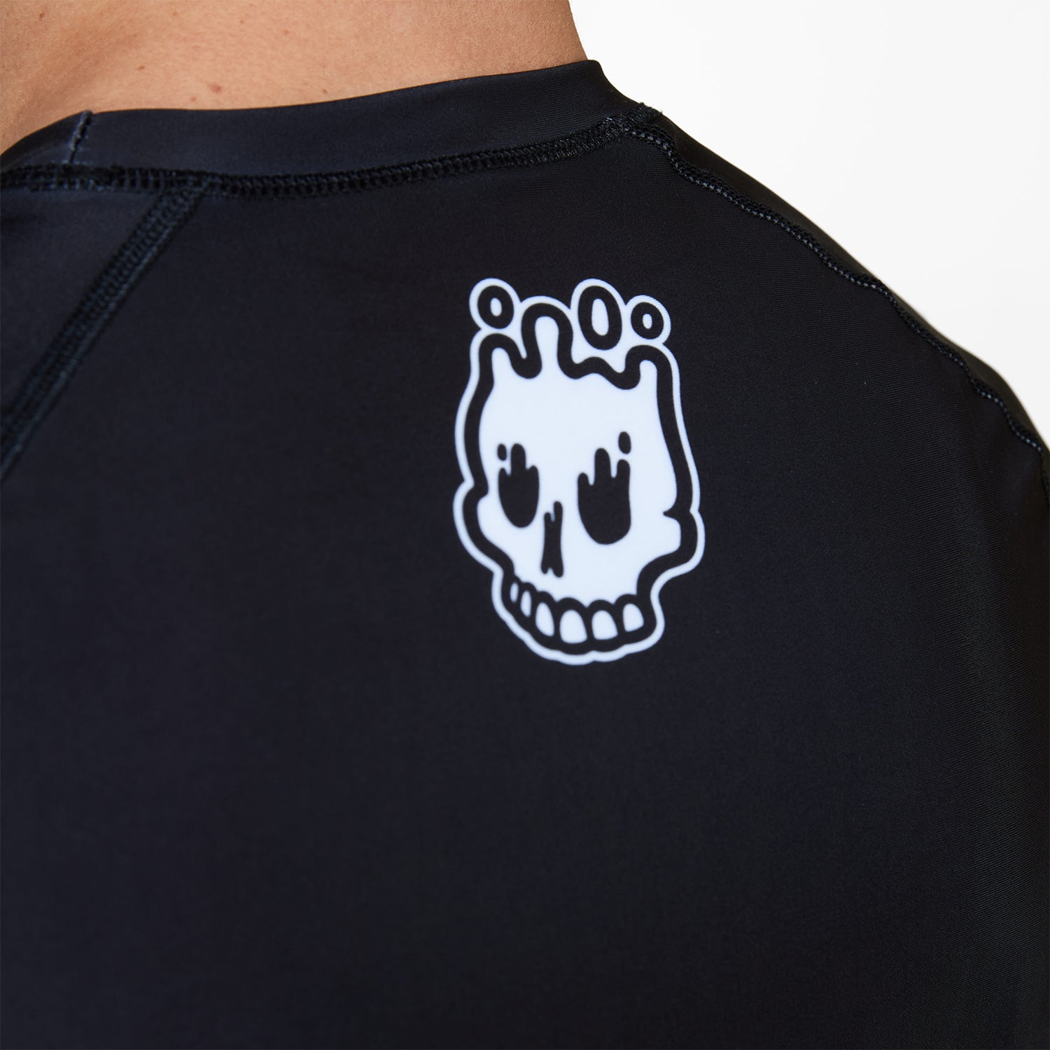 Close-up of melting skull Rubber Bones logo printed on the upper back of the Men’s Ash BJJ Rash Guard.
