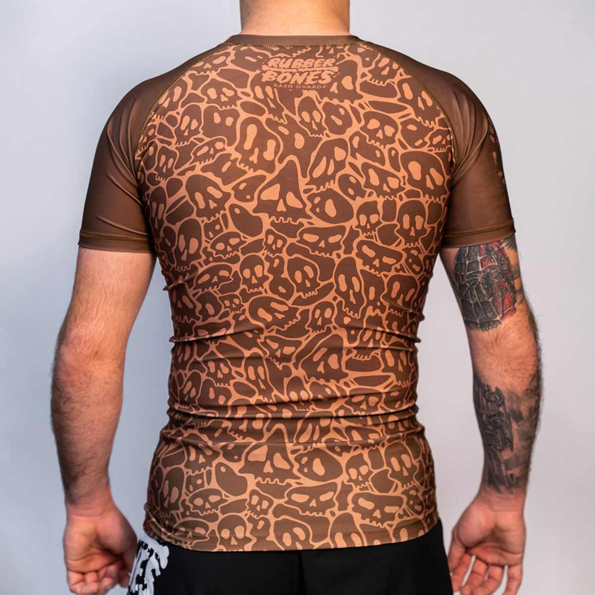 Back view of the Rubber Bones Ranked Brown BJJ rash guard – Brown compression rash guard featuring an all-over skull pattern and Rubber Bones branding on the upper back.