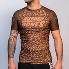 Front view of the Rubber Bones Ranked Brown BJJ rash guard – Brown short-sleeve rash guard with an all-over skull pattern and Rubber Bones logo on the chest.