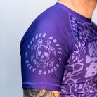 Close-up of the Rubber Bones Ranked Purple rash guard sleeve – Melting skull logo with 'Rubber Bones Rash Guards' text on a purple background.