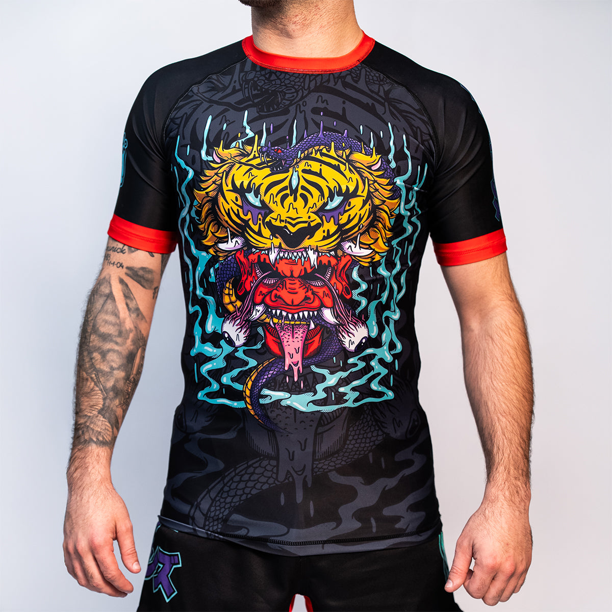 Front view of the Rubber Bones Tora Oni men's rash guard – Black no-gi rash guard featuring a tiger-demon graphic, red sleeve cuffs, and an athletic fit.