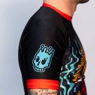 Close-up of the Rubber Bones Tora Oni men's rash guard sleeve – Teal melting skull graphic on a black background with red stitching.