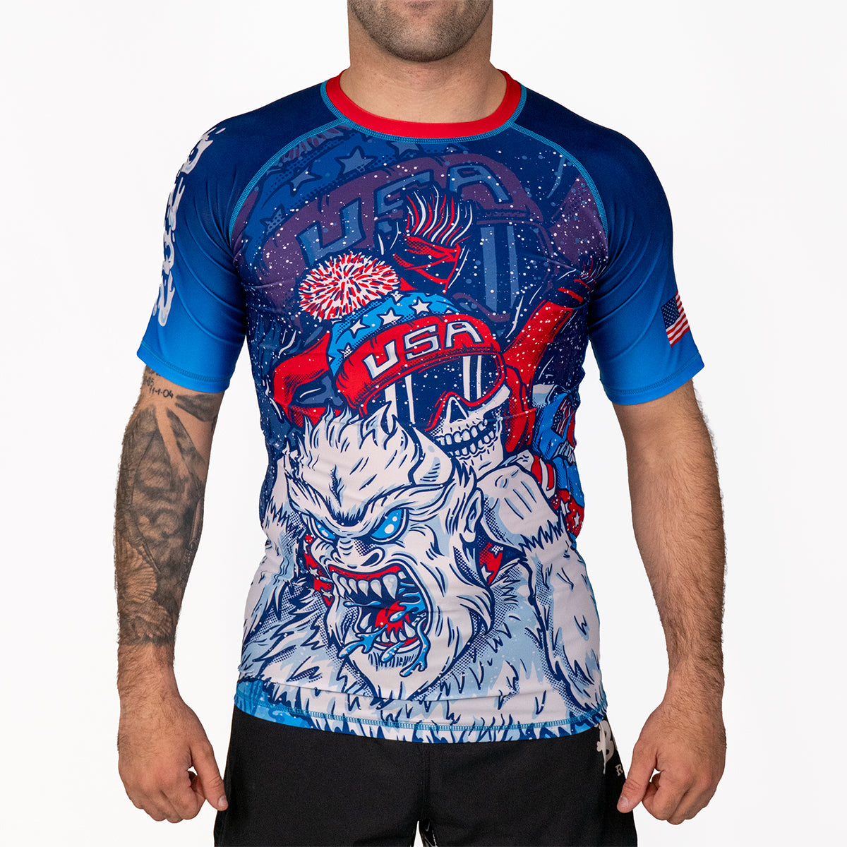 Men's Yeti Games short sleeve rash guard front view with skeleton skier choking Yeti artwork in patriotic red, white, and blue, USA flag patch on sleeve, compression fit.
