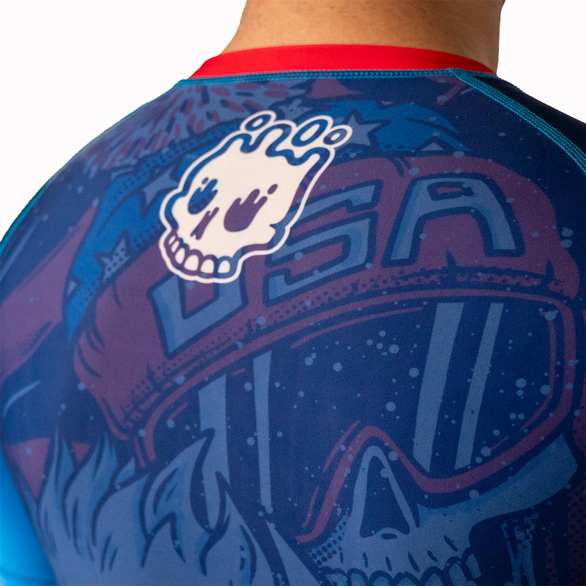 Back view close-up of Men's Yeti Games rash guard showing white Rubber Bones skull logo on navy and maroon gradient design with flatlock stitching detail.