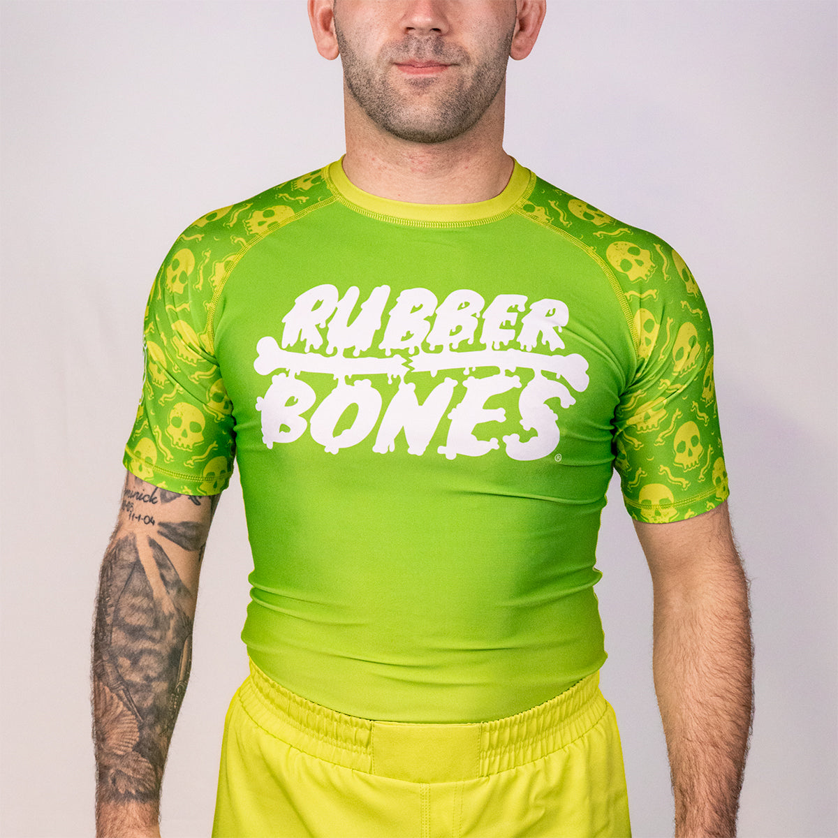 Front view of the Rubber Bones Poison Apple men’s BJJ rash guard with bright green body and skull print sleeves from the Deadly Harvest Collection.