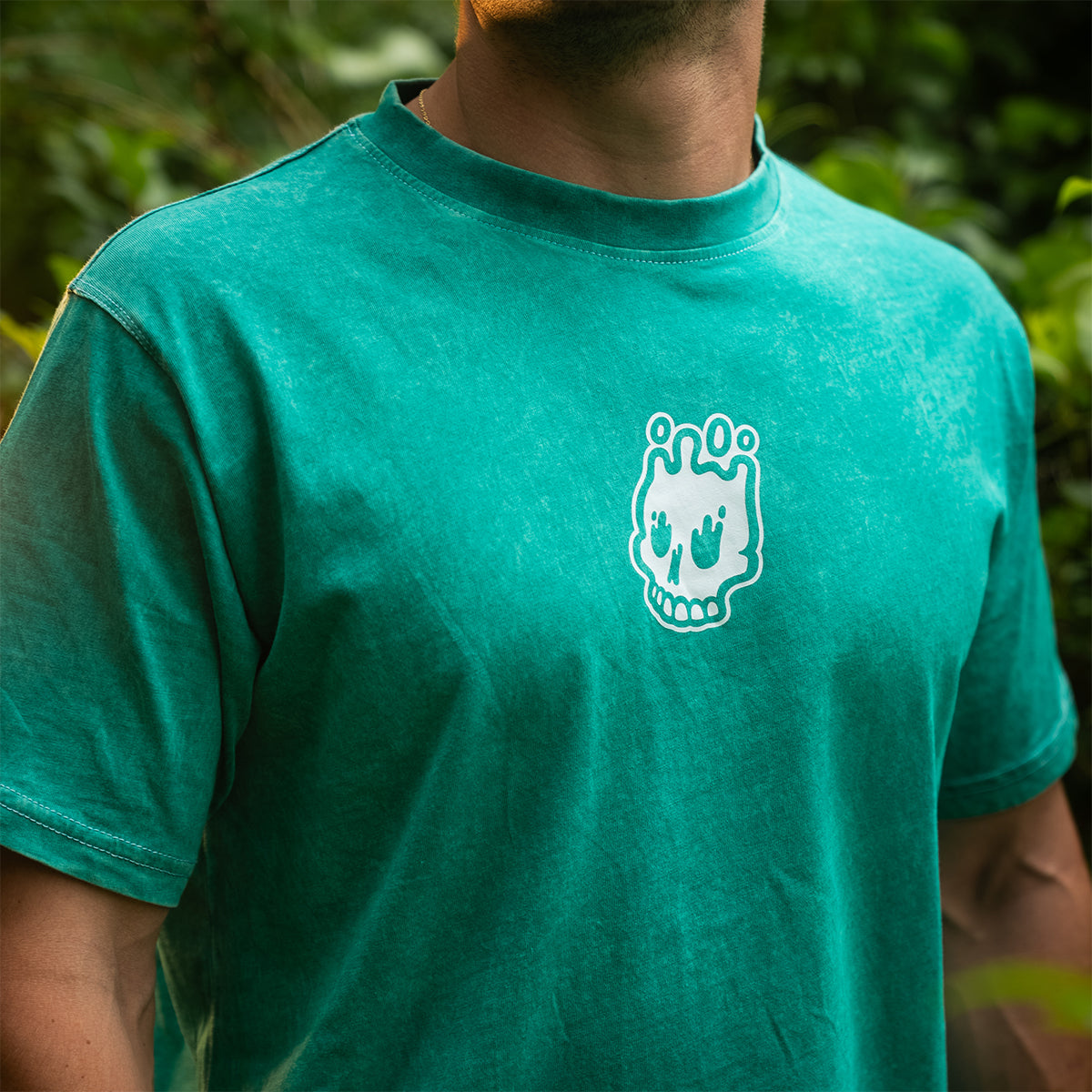 Close-up of a man wearing a teal mineral wash t-shirt with the Rubber Bones logo printed on the chest. Limited edition streetwear tee.