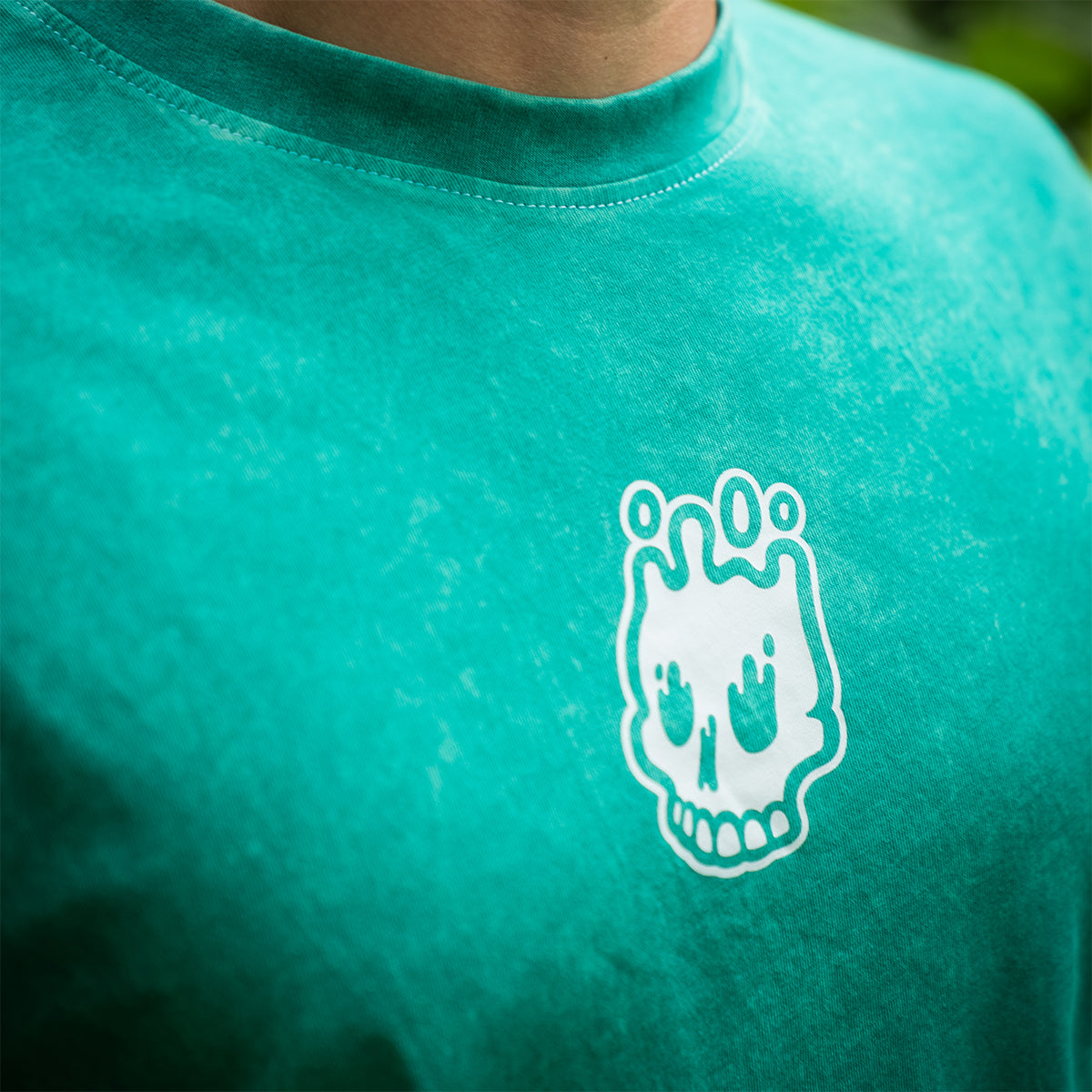 Side close-up of the Rubber Bones skull icon printed on a teal mineral wash t-shirt. Unique limited release streetwear tee.